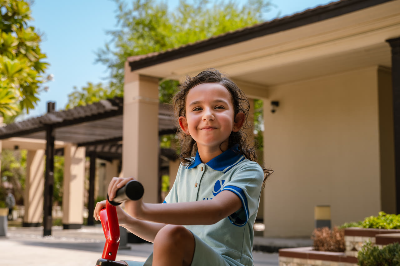 An Alphera learner pauses with a scooter in the courtyard.