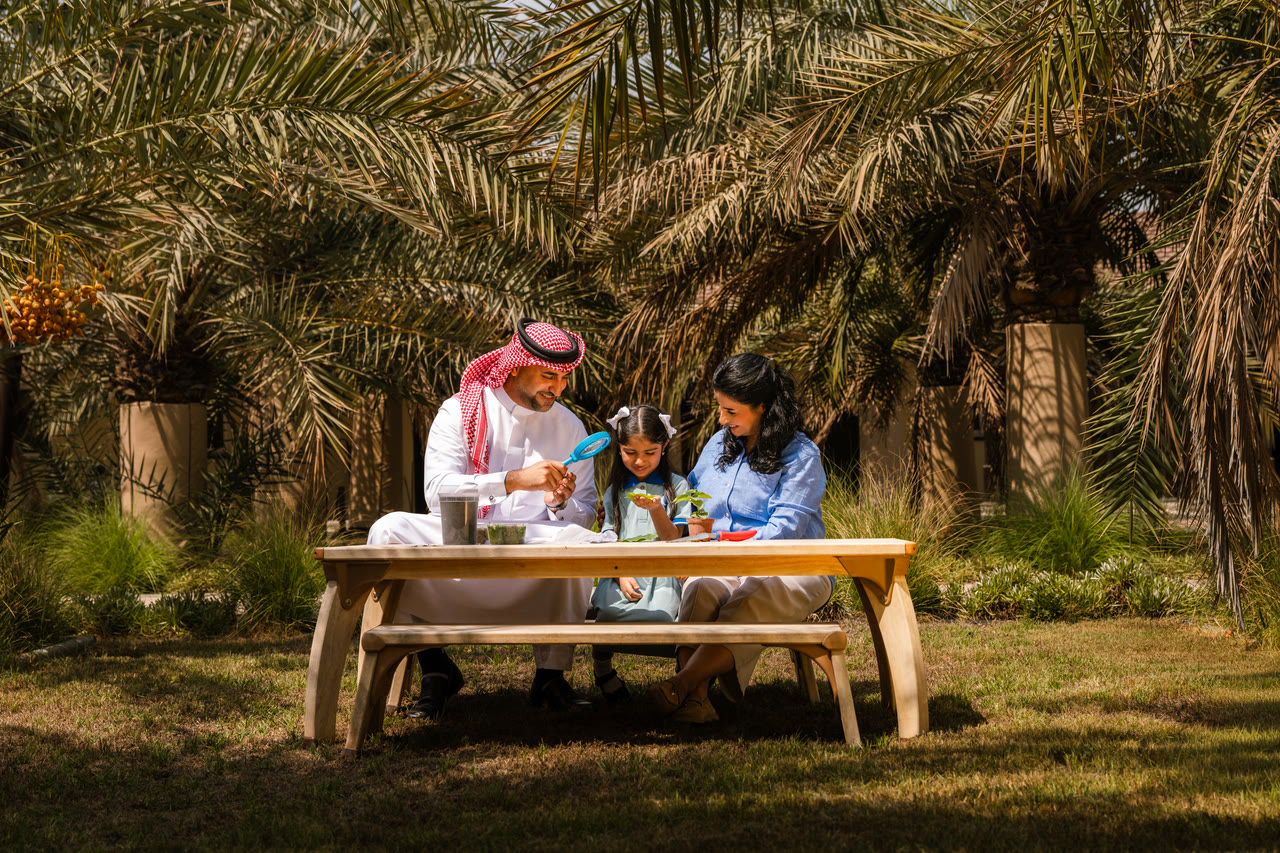 A family examines a plant together in the school garden.